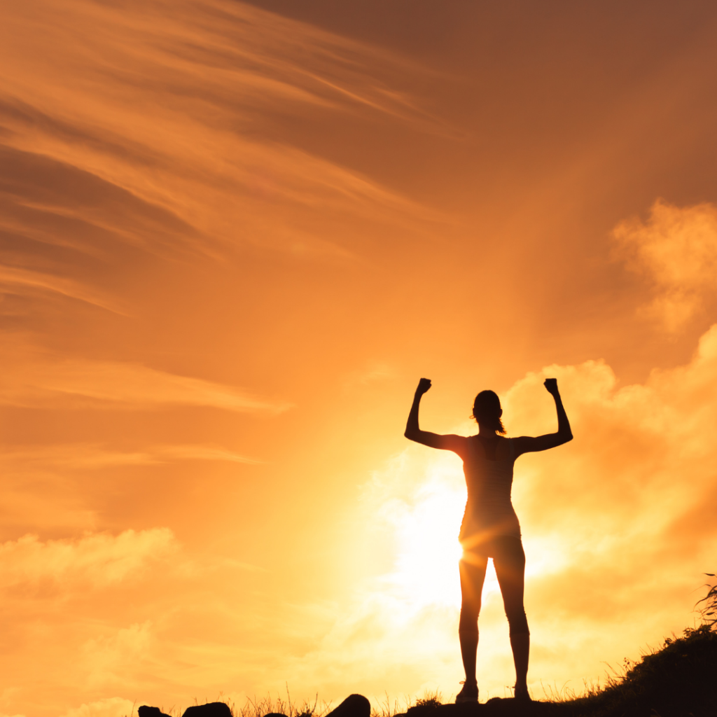 Image of a person standing on top of a mountain flexiing. This picture represents the strength it took Louise to work with her grief and to advocate for herself.