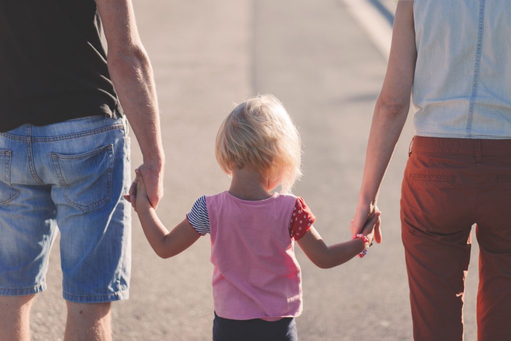 Image of a family outdoors. Two people are holding hands with a little kids, representing how spending time with family really does Louise a lot of good.