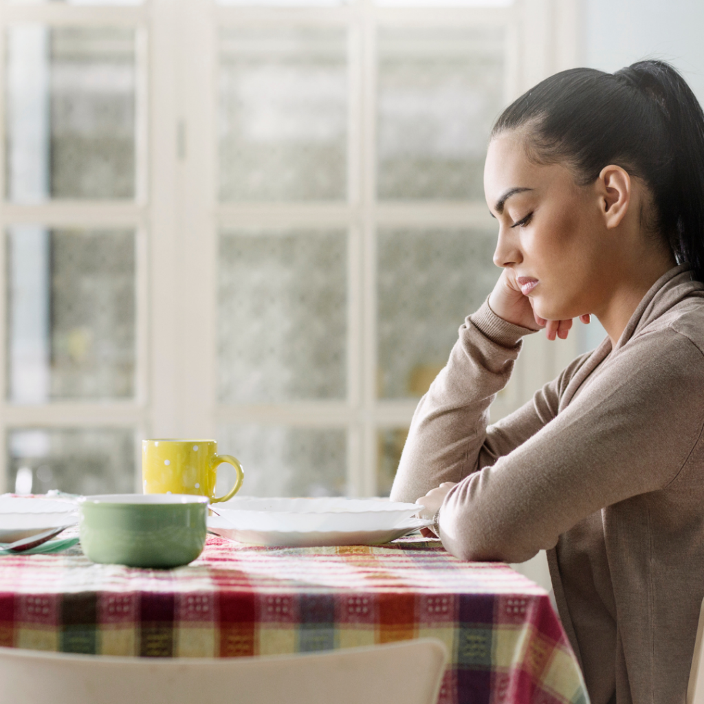 Image of a person with brown hair sitting at an empty kitchen table, representing the feelings of loneliness that often accompany living with Lichen Sclerosus.