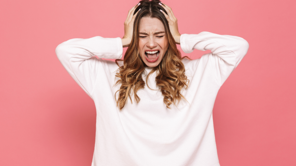 Image of a person with medium length brown hair with their hands on their heads screaming. This image represents the stress and mental health issues many of us go through with Lichen Sclerosus.