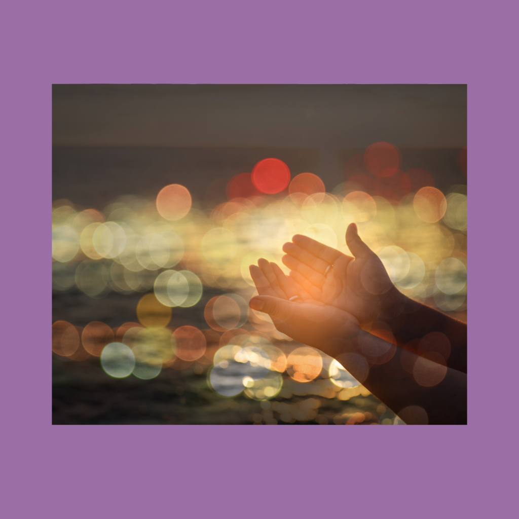 Outstretched palms with pinky sides resting against each other, with the forearms extending from the lower left corner to the center where the hands meet. Fuzzy orbs of multicolored lights dance across the background. The image has a purple border.