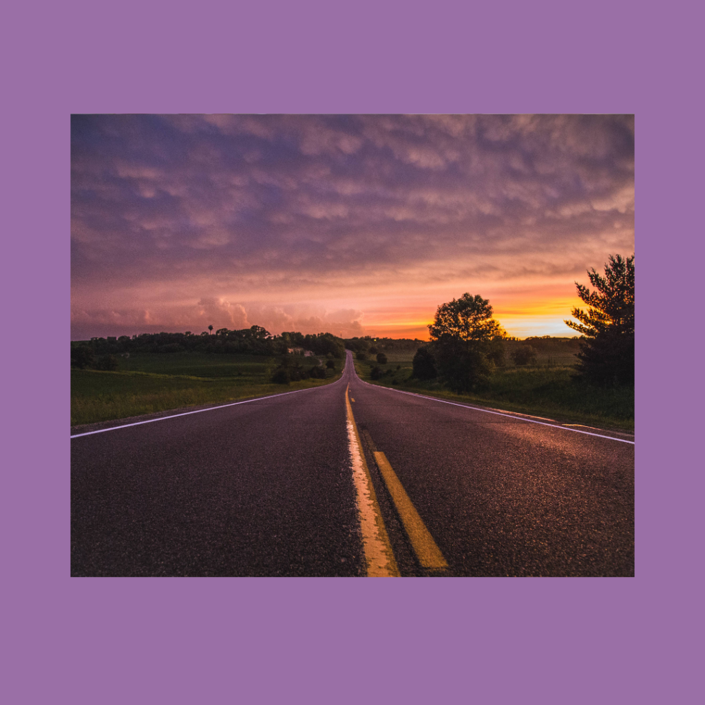 A golden sunset with fluffy overcast clouds above a long gray asphalt road that stretches into the horizon. The road is lined with green grass down one side sparse trees and green grass down the other, with more trees in the background lining the horizon. The image has a medium width purple border and the title text reads, "My Dilator Journey Part 2" in black font at the bottom.